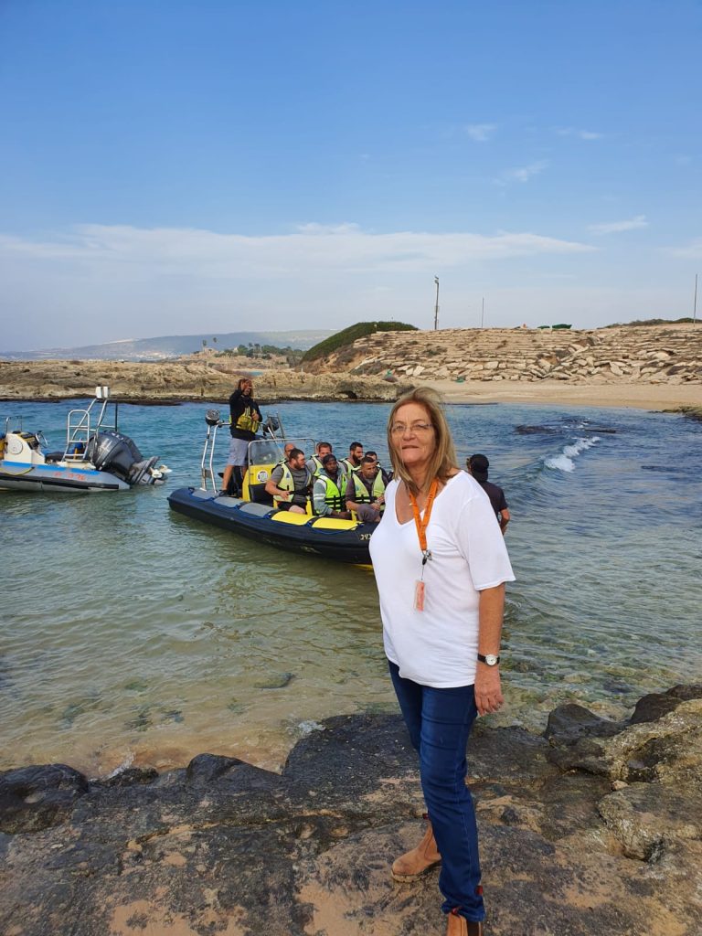 דודי אלבז מדריכת טיולים על חוף הים ליד סירת מטיילים